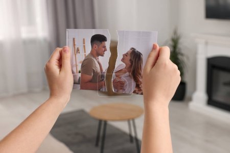 Woman holding torn photo in room, closeup. Divorce concept