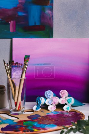 Téléchargez les photos : Canvas with gradient painting, brushes in glass and wooden artist's palette on table - en image libre de droit
