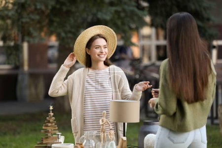 Women shopping on garage sale near table with different items in yard