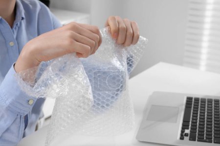 Photo for Woman popping bubble wrap at table in office, closeup. Stress relief - Royalty Free Image