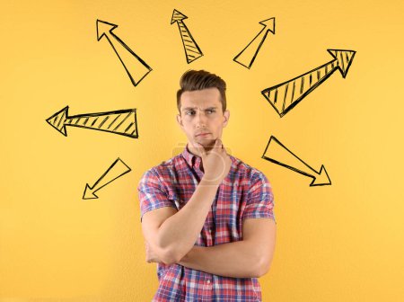 Foto de Choice in profession or other areas of life, concept. Making decision, thoughtful young man surrounded by drawn arrows on yellow background - Imagen libre de derechos