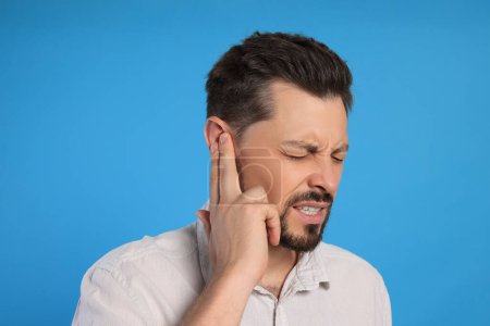 Photo for Man suffering from ear pain on light blue background - Royalty Free Image