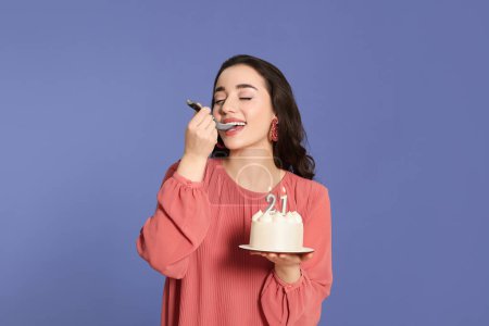 Foto de Coming of age party - 21st birthday. Smiling woman tasting delicious cake with number shaped candles on violet background - Imagen libre de derechos