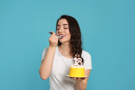 Coming of age party - 18th birthday. Woman tasting delicious cake with number shaped candles on light blue background
