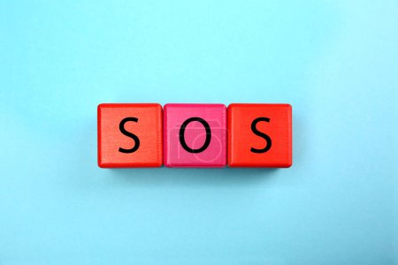 Foto de Abbreviation SOS (Save Our Souls) made of color cubes with letters on light blue background, top view - Imagen libre de derechos