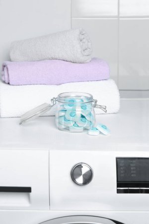 Photo for Jar with water softener tablets near stacked towels on washing machine - Royalty Free Image