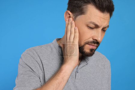 Mann leidet unter Ohrenschmerzen auf hellblauem Hintergrund