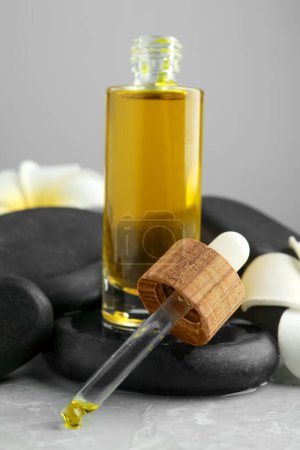 Photo for Bottle of face serum with spa stones and beautiful flowers on light grey table, closeup - Royalty Free Image