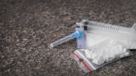Téléchargez les photos : Plastic bag with powder, syringe and pills on stone surface, space for text. Hard drugs - en image libre de droit