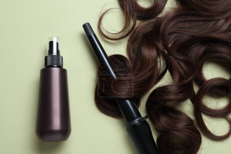 Photo for Spray bottle with thermal protection, lock of brown hair and stylish curling iron on pale green background, flat lay - Royalty Free Image
