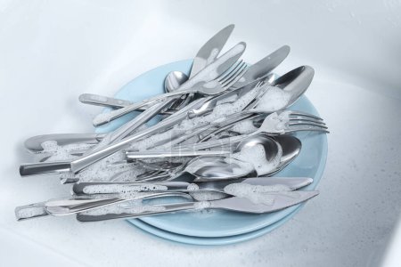 Téléchargez les photos : Washing silver spoons, forks and knives in foam - en image libre de droit