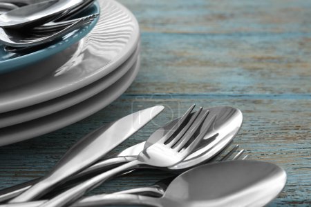 Foto de Silver clean spoons, forks and knives with plates on old light blue wooden table, closeup - Imagen libre de derechos