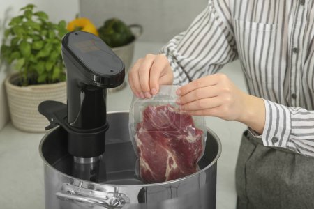 Woman putting vacuum packed meat into pot in kitchen, closeup. Thermal immersion circulator for sous vide cooking