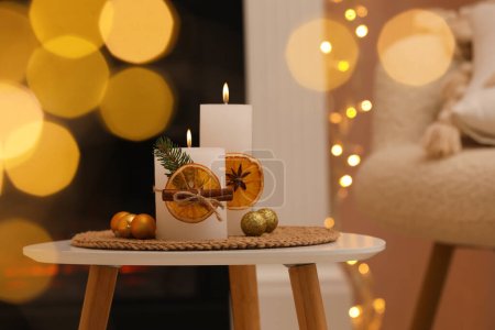 Foto de Hermosas velas encendidas decoradas con rebanadas de naranja seca y palitos de canela en la mesa blanca en el interior. Ambiente navideño - Imagen libre de derechos