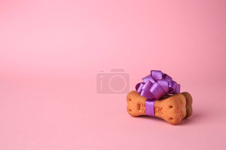 Téléchargez les photos : Bone shaped dog cookies with purple bow on pink background. Space for text - en image libre de droit
