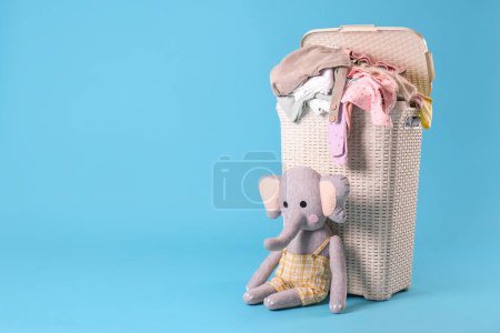 Photo for Laundry basket with baby clothes and soft toy on light blue background. Space for text - Royalty Free Image