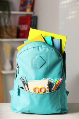 Foto de Turquoise backpack with different school stationery on white table indoors - Imagen libre de derechos