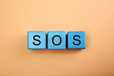 Foto de Abbreviation SOS (Save Our Souls) made of light blue cubes with letters on pale coral background, top view - Imagen libre de derechos
