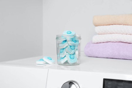 Téléchargez les photos : Pot avec des comprimés d'adoucissant d'eau près de serviettes empilées sur la machine à laver - en image libre de droit