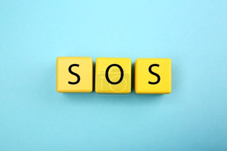 Foto de Abbreviation SOS (Save Our Souls) made of yellow cubes with letters on light blue background, top view - Imagen libre de derechos