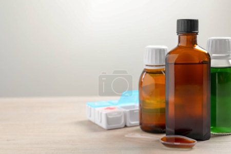 Téléchargez les photos : Bottles of syrup, dosing spoon and weekly pill organizer on table against white background, space for text. Cold medicine - en image libre de droit