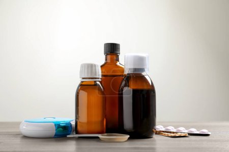 Téléchargez les photos : Bottle of syrup, dosing spoon and pills on table against light background. Cold medicine - en image libre de droit