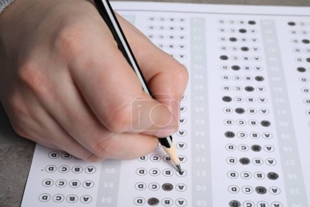 Téléchargez les photos : Student filling answer sheet at table, closeup. Passing exam - en image libre de droit