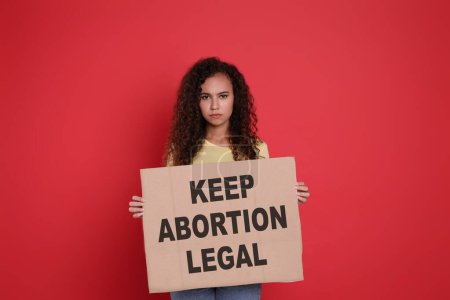Foto de African American woman holding placard with phrase Keep Abortion Legal on red background. Abortion protest - Imagen libre de derechos