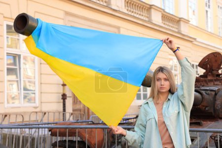 Téléchargez les photos : Sad woman holding Ukrainian flag near broken tank in city - en image libre de droit