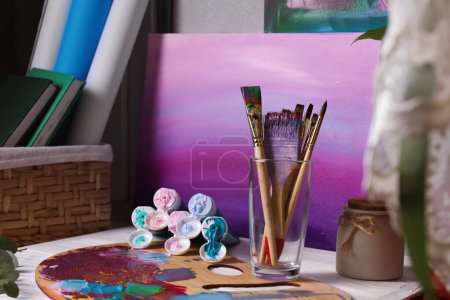 Téléchargez les photos : Wooden artist's palette with colorful paints, brushes and scented candle on white table - en image libre de droit