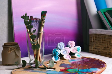 Foto de Wooden artist's palette with colorful paints, brushes and scented candle on white table - Imagen libre de derechos