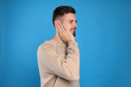 Photo for Young man suffering from ear pain on light blue background - Royalty Free Image