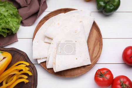 Photo for Delicious folded Armenian lavash and fresh vegetables on white wooden table, flat lay - Royalty Free Image