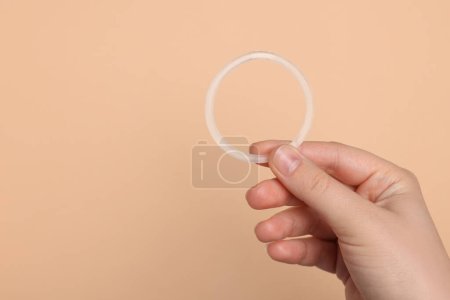 Téléchargez les photos : Woman holding diaphragm vaginal contraceptive ring on beige background, closeup. Space for text - en image libre de droit