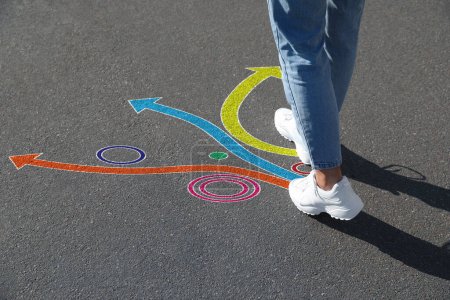 Foto de Choice of way. Woman walking towards drawn marks on road, closeup. Colorful arrows pointing in different directions - Imagen libre de derechos