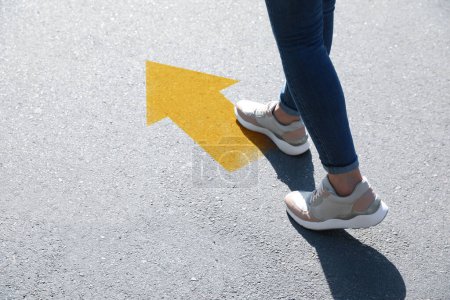 Planning future. Woman walking to drawn mark on road, closeup. Yellow arrow showing direction of way