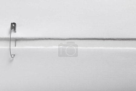 Pieces of paper sheets joined with safety pin on white background, top view