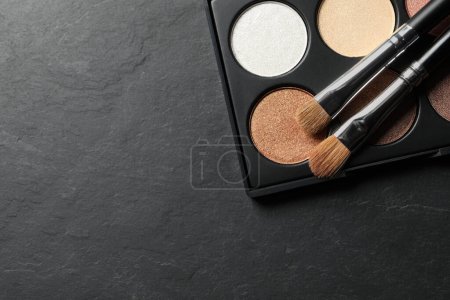 Photo for Beautiful eye shadow palette with brushes on dark grey textured table, top view. Space for text - Royalty Free Image