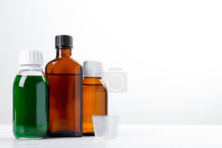 Téléchargez les photos : Bottles of syrups with measuring cup on wooden table against white background, space for text. Cough and cold medicine - en image libre de droit