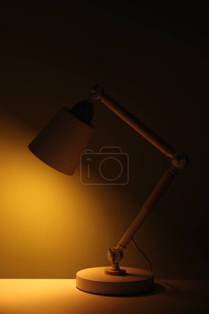 Téléchargez les photos : Stylish modern desk lamp on table at night - en image libre de droit