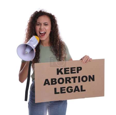Foto de Emotional African American woman shouting into megaphone and holding placard with phrase Keep Abortion Legal on white background. Abortion protest - Imagen libre de derechos