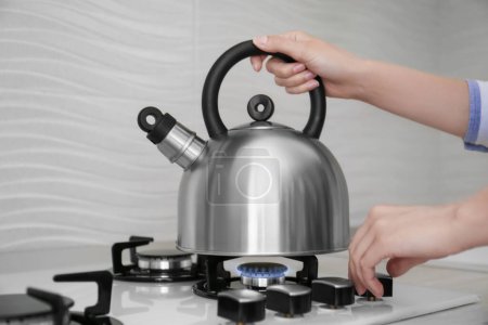 Photo for Woman putting kettle on gas stove in kitchen, closeup - Royalty Free Image