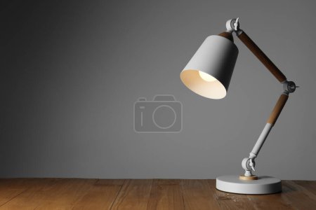 Téléchargez les photos : Stylish modern desk lamp on wooden table against grey background, space for text - en image libre de droit