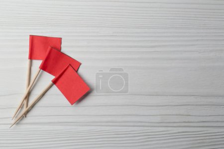 Small red paper flags on white wooden table, flat lay. Space for text
