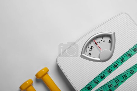 Foto de Weight loss concept. Scales, dumbbells and measuring tape on white background, flat lay. Space for text - Imagen libre de derechos