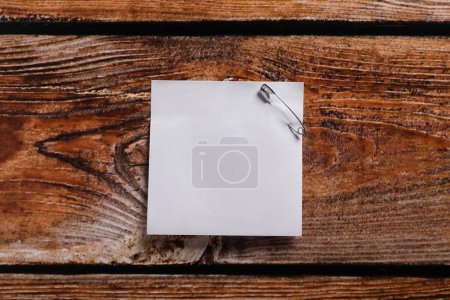 Téléchargez les photos : Paper sheet attached with safety pin on wooden table, top view. Space for text - en image libre de droit