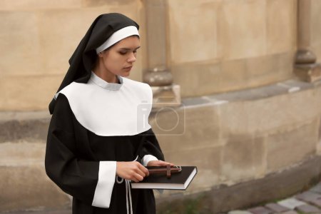 Téléchargez les photos : Young nun with Christian cross and Bible near building outdoors, space for text - en image libre de droit