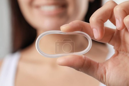 Téléchargez les photos : Woman holding diaphragm vaginal contraceptive ring on blurred background, closeup - en image libre de droit
