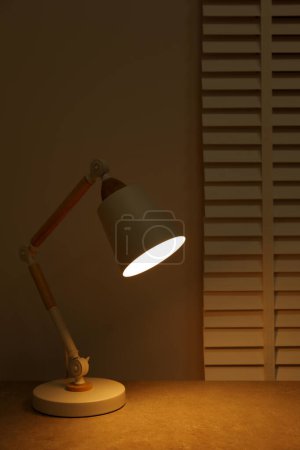 Téléchargez les photos : Stylish modern desk lamp on table at night - en image libre de droit
