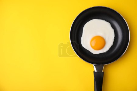 Tasty fried egg in pan on yellow background, top view. Space for text
